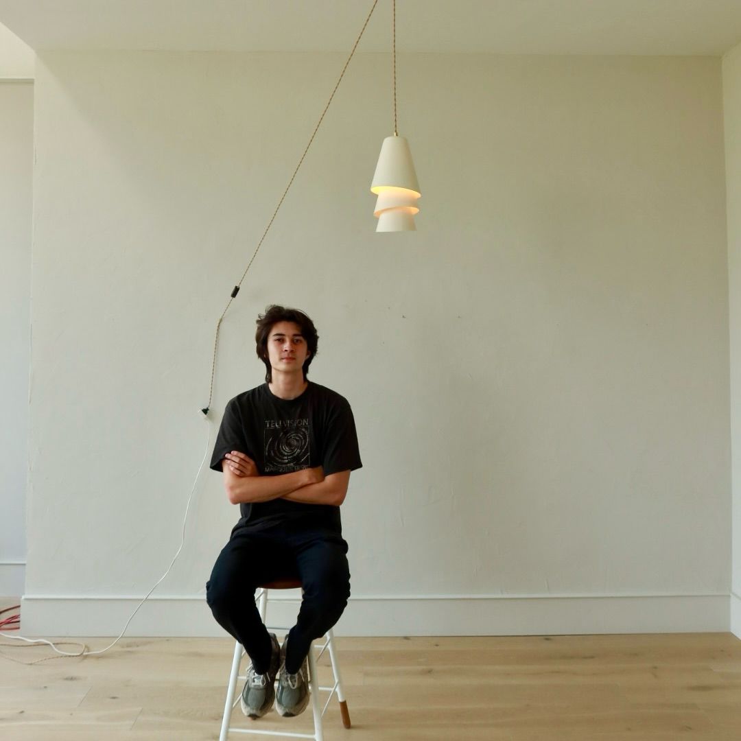 Otis Harrison seated beneath his lit Blossom Pendant in a bare white room